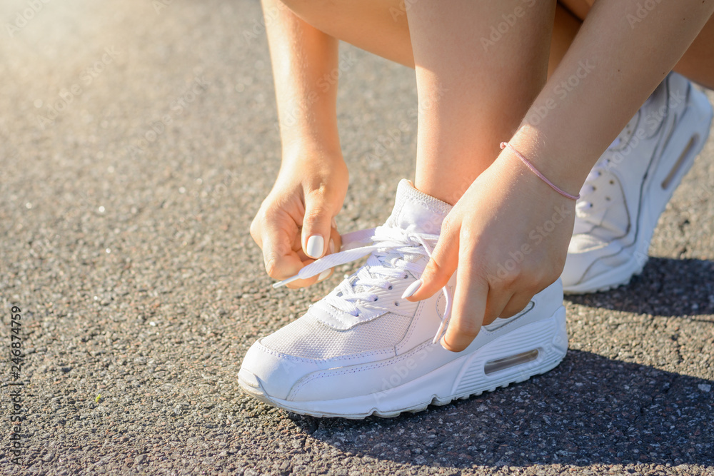 Young teenage girl in white sneakers typing shoelaces before running in the morning on asphalt road in the countryside