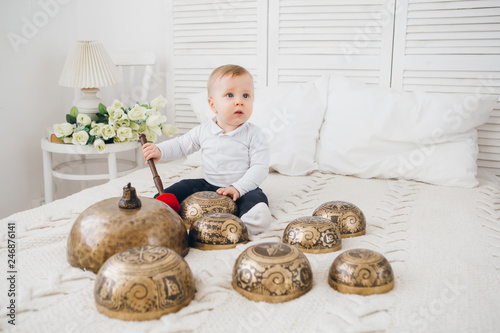 Little boy playing with Tibetan singing bowls sitting on the bed