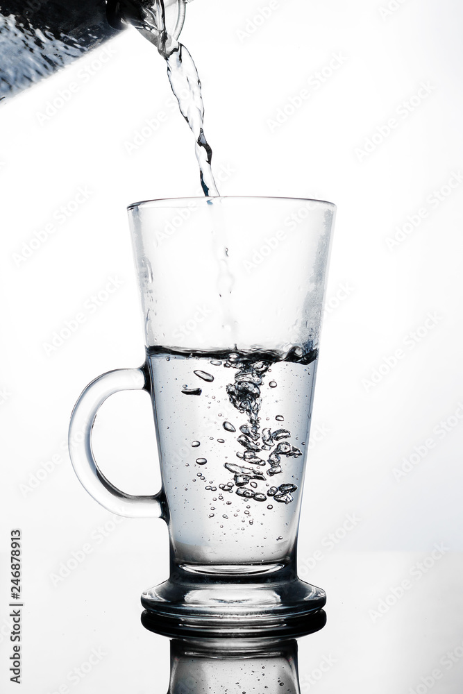 Hand pours water into a glass glass Cup of glass teapot. Shut. Isolated on white background Hand pours water into a glass glass Cup of glass teapot. Shut. Isolated on white background
