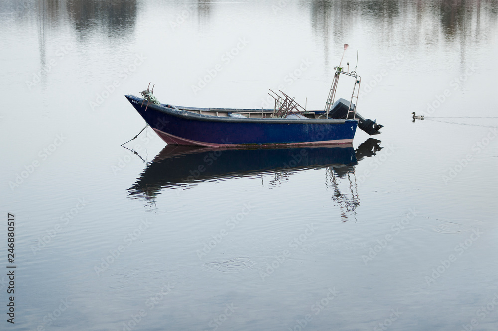 Blue fishing boat stopped in the water with reflection