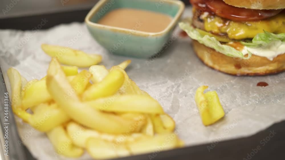 A close-up with burger fixed with a stick, and sauce boat with tomato sauce. The camera moves to the left right and stops at the French fries lying in the corner of the tray A close-up with burger fixed with a stick, and sauce boat with tomato sauce. The camera moves to the left right and stops at the French fries lying in the corner of the tray