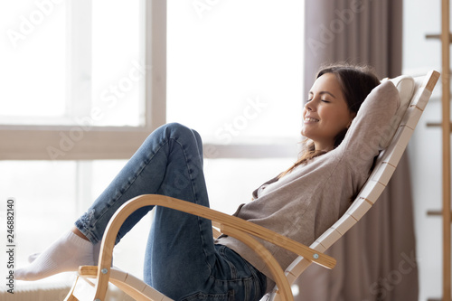Relaxed calm young woman lounging sitting in comfortable wooden rocking chair breathing fresh air dreaming, happy lazy girl chilling relaxing enjoying no stress free peaceful quiet weekend at home