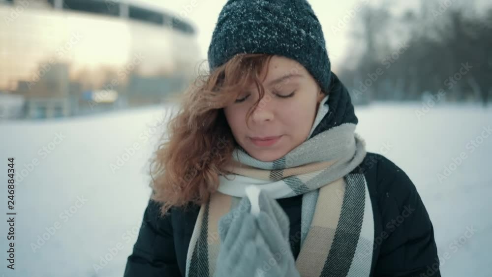 Sick young woman blows her nose using paper handkerchief outdoors on snowy winter day. Sick young woman blows her nose using paper handkerchief outdoors on snowy winter day.