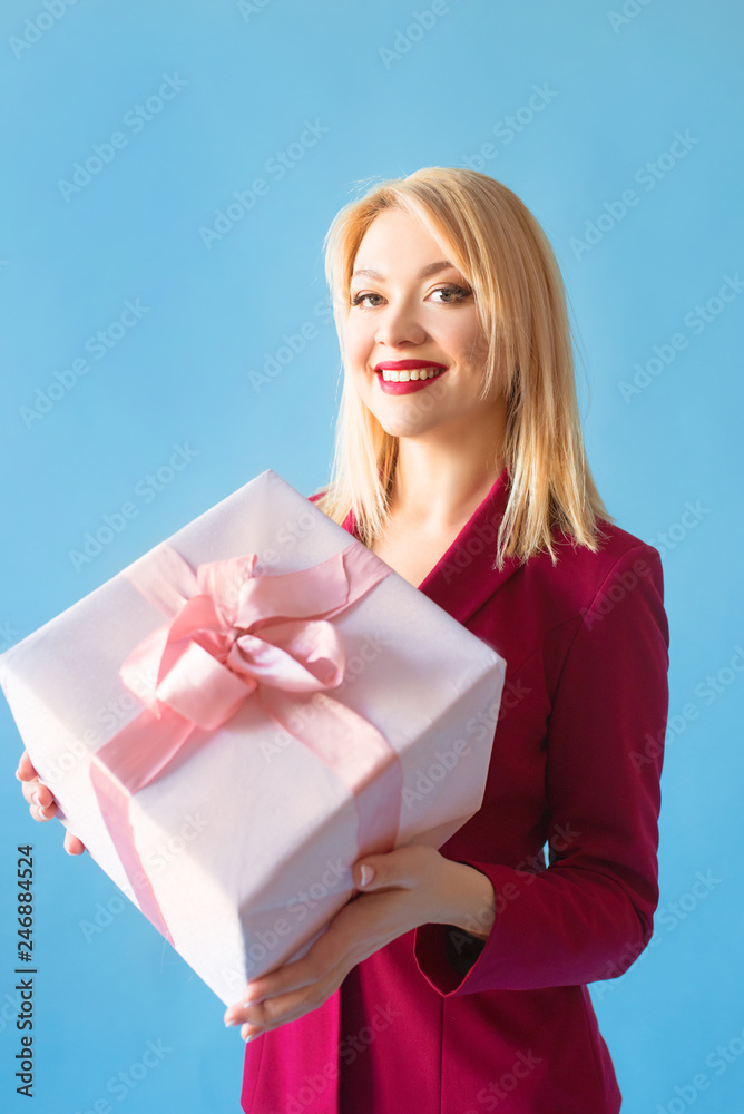 beautiful smiling blonde woman in blazer with present box in her arms on blue background beautiful smiling blonde woman in blazer with present box in her arms on blue background