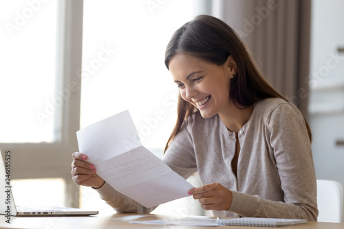 Happy excited woman student customer reading letter with good news, great cheap offer, get job opportunity, scholarship admission, loan approval, money refund holding paper mail bank statement photo