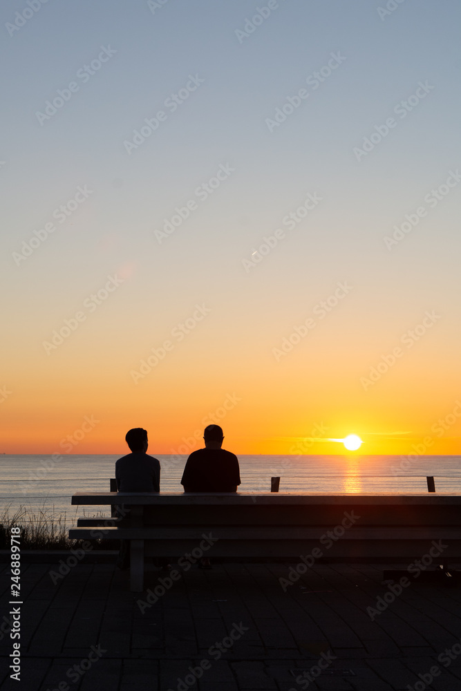 A couple enjoying the beautiful sunset at the dunes in the Netherlands, sitting on a bench.