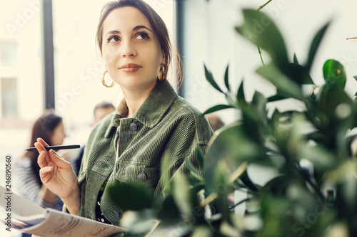 Woman stand at office surround with green plants and write at her note book