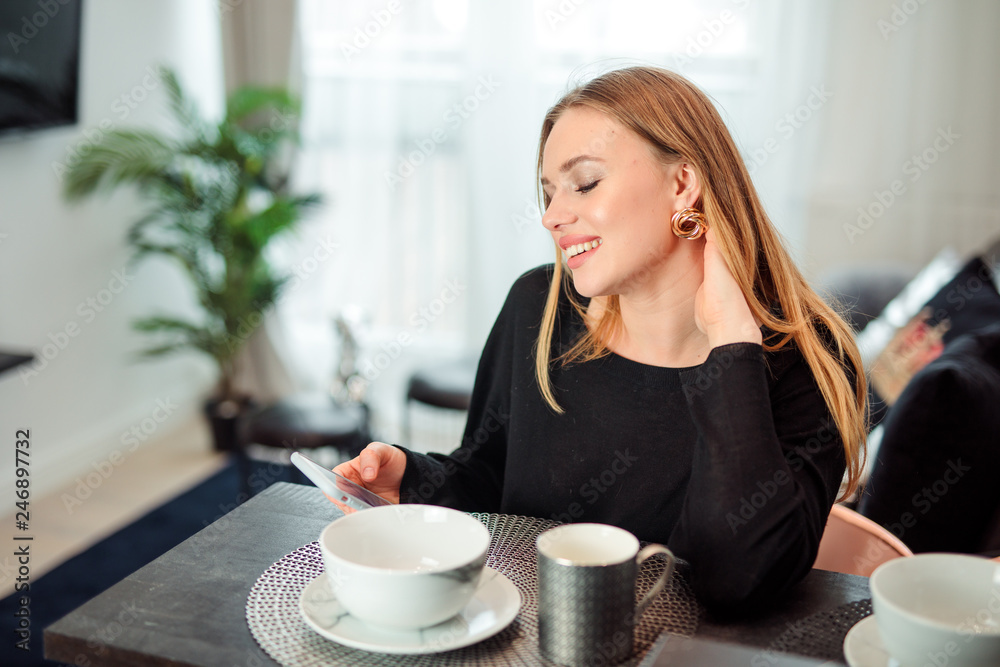 Blonde girl sit at the kitchen drink coffee and talking at her phone. Blonde girl sit at the kitchen drink coffee and talking at her phone.