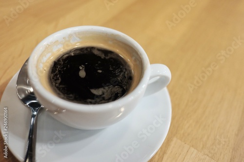 Close up a hit expresso coffee In a white cup with steel spoon on wooden dinning table at night with warm light