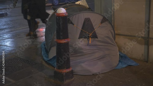 A homeless person in a tent in a city on a snowy night.