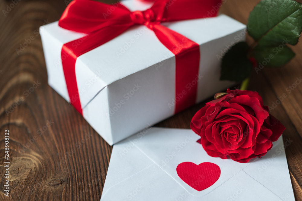 Beautiful red rose on a dark wooden background. White envelope with a red heart. White gift box tied with a red ribbon. Valentine's Day. March 8. Mothers Day. holidays. birthday. Santa. new Year. Chri Beautiful red rose on a dark wooden background. White envelope with a red heart. White gift box tied with a red ribbon. Valentine's Day. March 8. Mothers Day. holidays. birthday. Santa. new Year. Chri