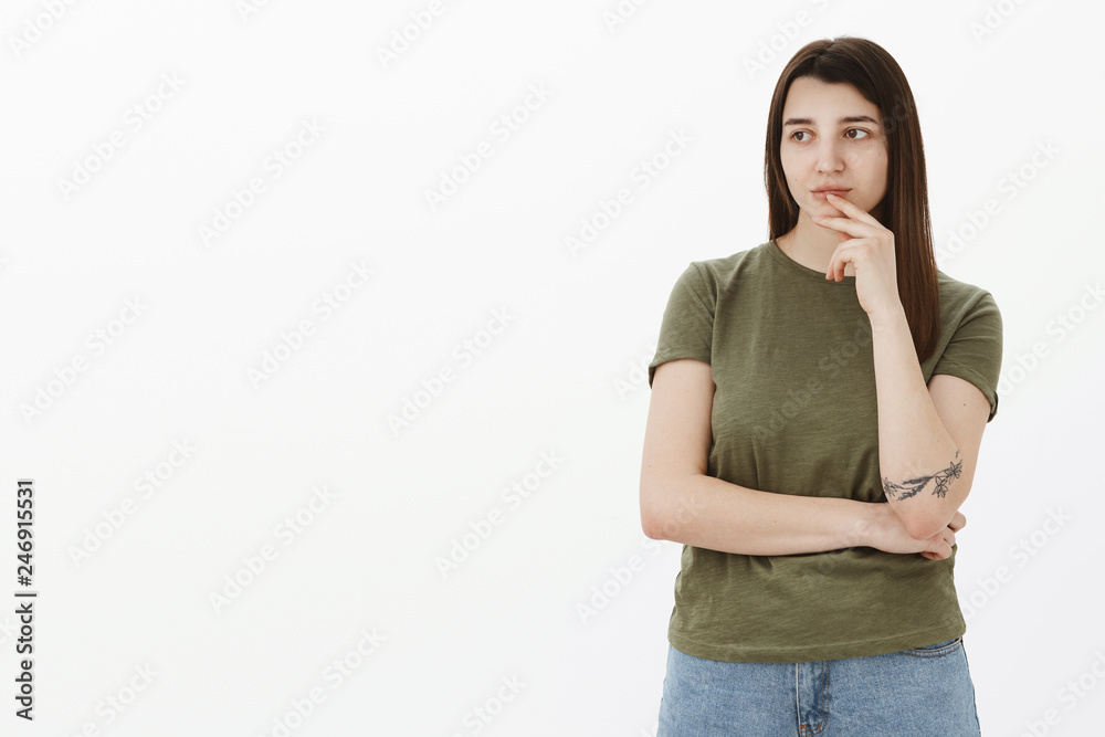 Girl deep thinking spacing out as looking with interest, thoughtful at left side of copy space touching lip with finger cross arm over body looking determined and judgemental over gray background Girl deep thinking spacing out as looking with interest, thoughtful at left side of copy space touching lip with finger cross arm over body looking determined and judgemental over gray background