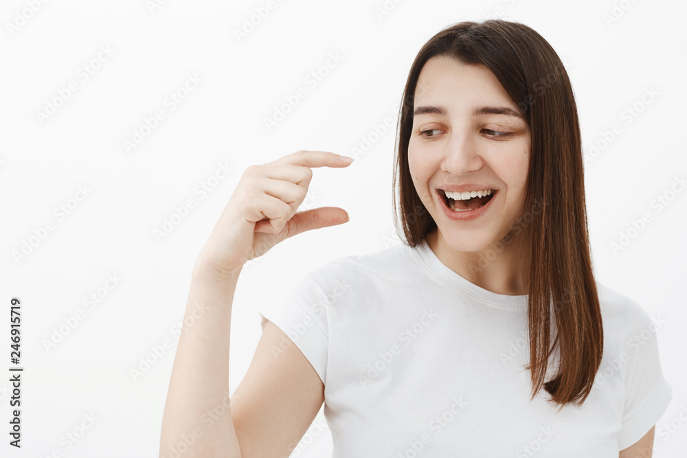 Close-up shot of amused and happy upbeat brunette in 20s laughing out loud and smiling delighted as shaping something tiny or small and looking and hand with grin over gray background Close-up shot of amused and happy upbeat brunette in 20s laughing out loud and smiling delighted as shaping something tiny or small and looking and hand with grin over gray background