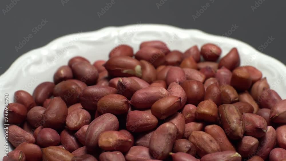 Raw unpeeled peanuts. Rotation. Snack closeup. Peanuts in a bowl. Selective focus. grey background. Studio shot. Healthy food concept. Raw unpeeled peanuts. Rotation. Snack closeup. Peanuts in a bowl. Selective focus. grey background. Studio shot. Healthy food concept.