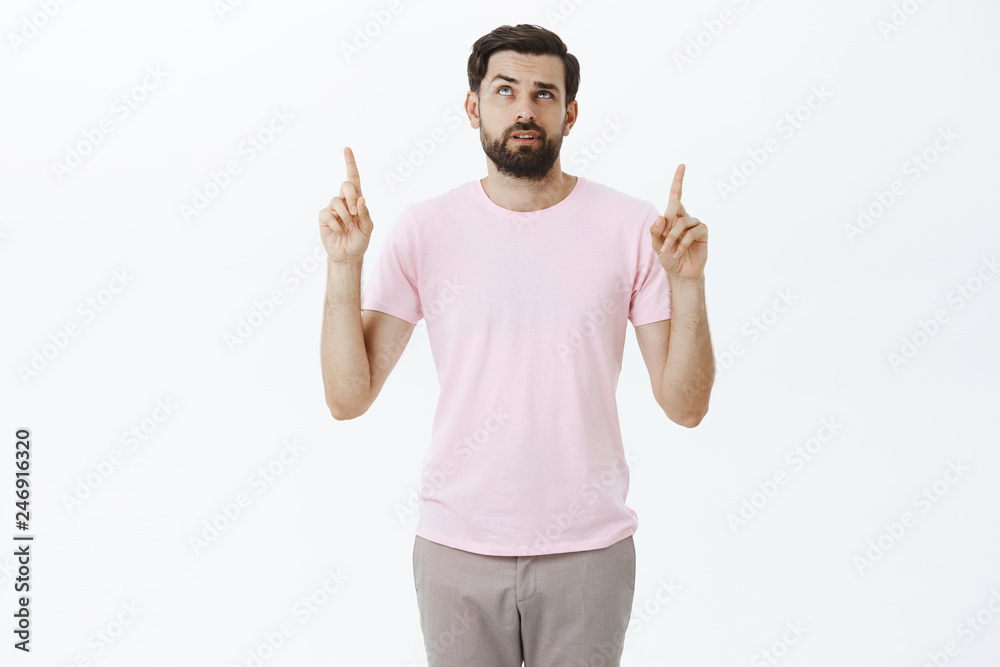 Unsure and confused man cannot get clue what written upwards, looking and pointing up raising eyebrow questioned and clueless, open mouth as cannot understand product, posing unaware over gray wall Unsure and confused man cannot get clue what written upwards, looking and pointing up raising eyebrow questioned and clueless, open mouth as cannot understand product, posing unaware over gray wall