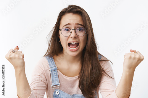 Cheerful excited and energized woman yelling in cheer and support clenching fists thrilled as yelling wanting favorite team win being true fan standing supportive over gray background