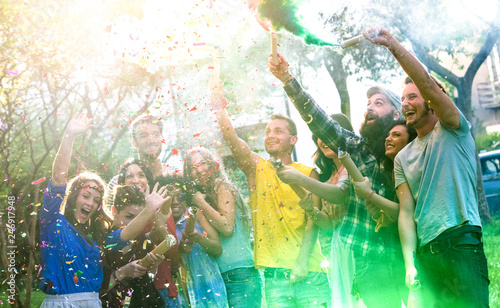 Happy millennial friends having fun at garden party with multicolored smoke bombs outside - Young millenial students celebrating spring break fest together on genuine youth concept - Focus on confetti © Mirko Vitali