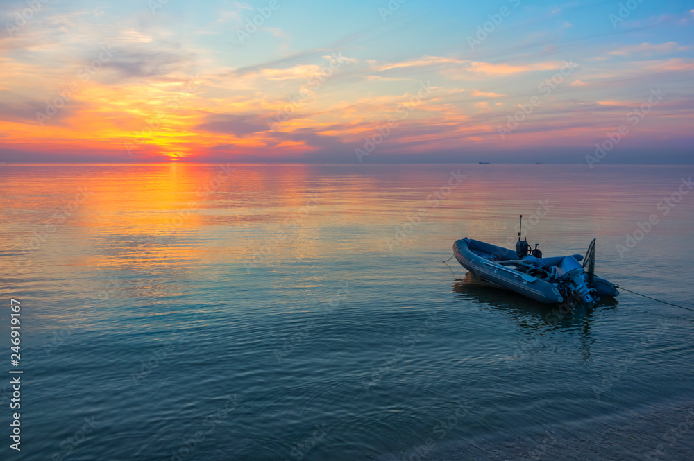 Fishing boat in the calm sea on a background of a beautiful sunset with ships on the horizon