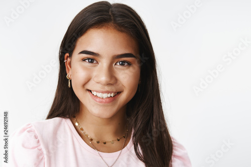 Headshot of nice sincere and gentle young teenage indian girl with earrings and neckles smiling broadly at camera feeling delighted and friendly posing carefree against gray background