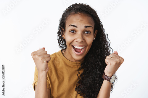 Delighted happy lucky african american girl receiving promotion feeling thrilled and satisfied clenching fists in success, celebrating victory smiling broadly from excitement as triumphing photo