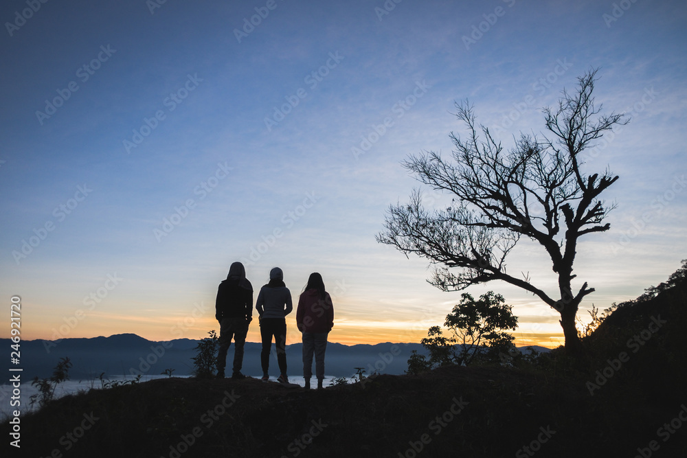 Three silhouette ​of people standing watching sunr​ise on the mountain in northern province of Thailand.