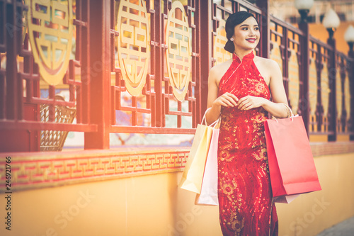 Chinese girl wearing Cheongsam and smile happily. Holding her shopping bags after a lot of shopping malls in Chinatown and was walking on the sidewalk. Amid the atmosphere of the evening sun. © brain2hands