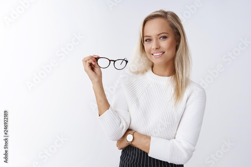 Woman trying new glasses in store picking right frame fits style posing over white background confident and satisfied smiling pleased holding eyewear in arm feeling self-assured and successful