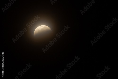 Fototapeta Naklejka Na Ścianę i Meble -  Full Lunar Eclipse in January 2019 is pictured in various stages of the eclipse. The bright white moon turns dark and black and eventually a yellowish orange that glows in the dark night sky