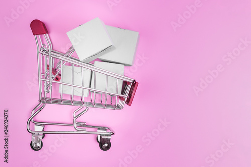 Shopping cart with boxes on pink background. The concept of delivering and online shop.