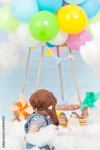 a small child looks at a bundle of colored balloons filled with helium tied to a wooden pilot basket. located in the sky among the clouds. heaven's decoration.