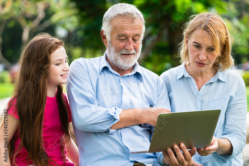 Happy family using laptop computer together in the garden park in summer. Kid education and family activities concept. photo