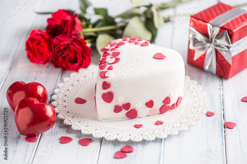 Marzipan white cake in the shape of a heart with red hearts. As the decoration bouquet of red roses a gift from the ribbon. Wedding or valentines day concept.