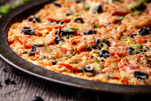 Concept of Italian cuisine, Homemade Italian pizza with salami sausage, tomatoes, with black olives and cheese on a wooden background. copy space