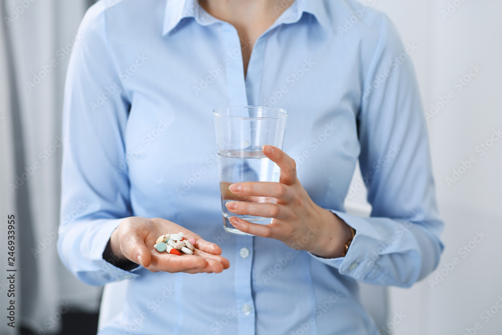 Young unknown woman holding pills and glass of water, closeup of hands. Medicine and healthcare concept Young unknown woman holding pills and glass of water, closeup of hands. Medicine and healthcare concept