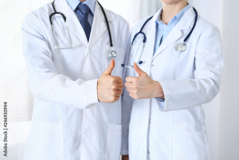 Team of unknown medicine doctors showing OK sign with thumb up close up. Success and high level service in health care, best treatment and customer loyalty and physical concept Team of unknown medicine doctors showing OK sign with thumb up close up. Success and high level service in health care, best treatment and customer loyalty and physical concept