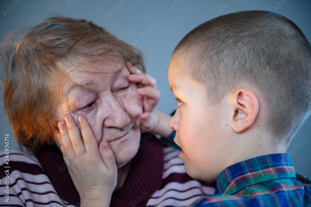 Elderly grandmother and grandson spend time together in green checkered shirt. Boy and the old woman are very attached to each other. Elderly grandmother and grandson spend time together in green checkered shirt. Boy and the old woman are very attached to each other.