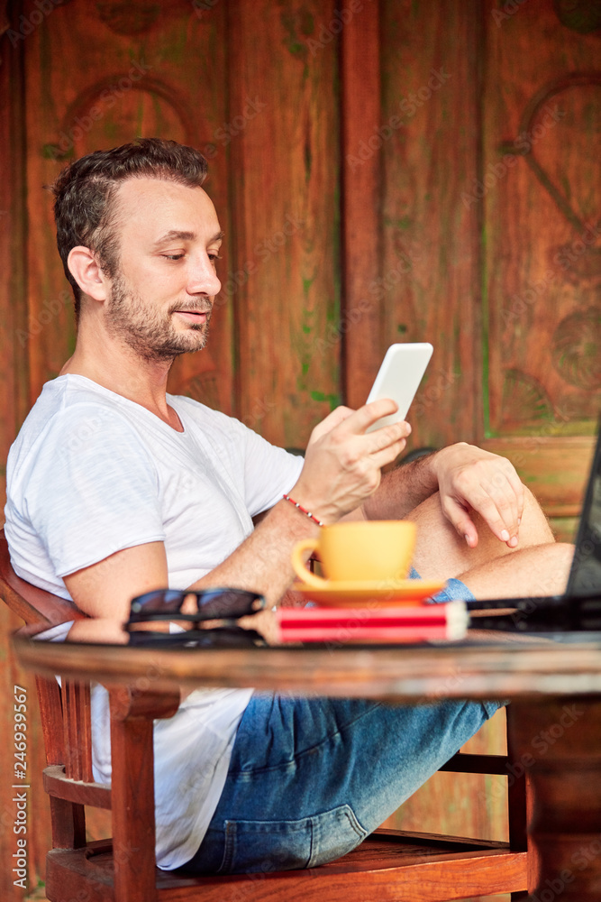 Man with smartphone, coffee / tea and laptop on a home porch. Man with smartphone, coffee / tea and laptop on a home porch.