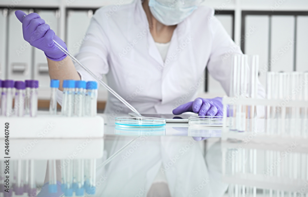 Close-up of professional female scientist in protective eyeglasses making experiment with reagents in laboratory. Medicine and research concept Close-up of professional female scientist in protective eyeglasses making experiment with reagents in laboratory. Medicine and research concept