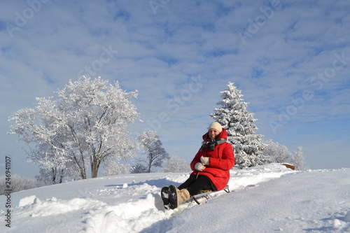 Happy young beautiful woman in a bright red jacket, hat and scarf on a sled on the background of a fabulous winter landscape on the mountain 