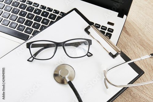 Modern medical technology and sofware advances concept. Doctor's working table with stethoscope acoustic device, laptop keyboard close up on wooden desktop. Copy space, background, top view, flat lay.