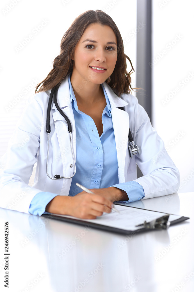 Doctor woman filling up medical form while sitting at the desk in hospital office. Physician at work. Medicine and health care concept Doctor woman filling up medical form while sitting at the desk in hospital office. Physician at work. Medicine and health care concept