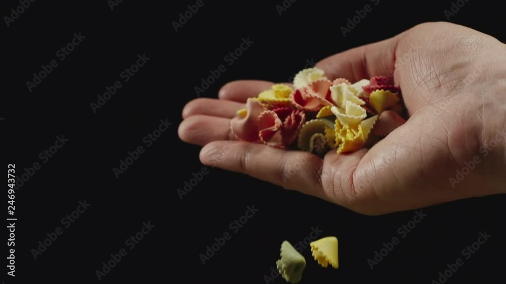 SLOW MOTION: Color figural pasta falling from a hand on a black background SLOW MOTION: Color figural pasta falling from a hand on a black background