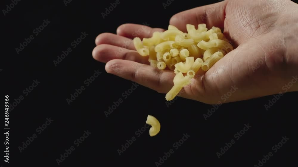 SLOW MOTION: Macaroni falling from a hand on a black background SLOW MOTION: Macaroni falling from a hand on a black background