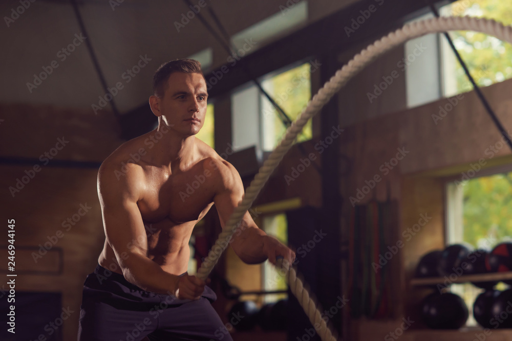 Fit, sporty and athletic sportsman working in a gym. Man training using battle ropes. Sports, athletics and fitness concept.