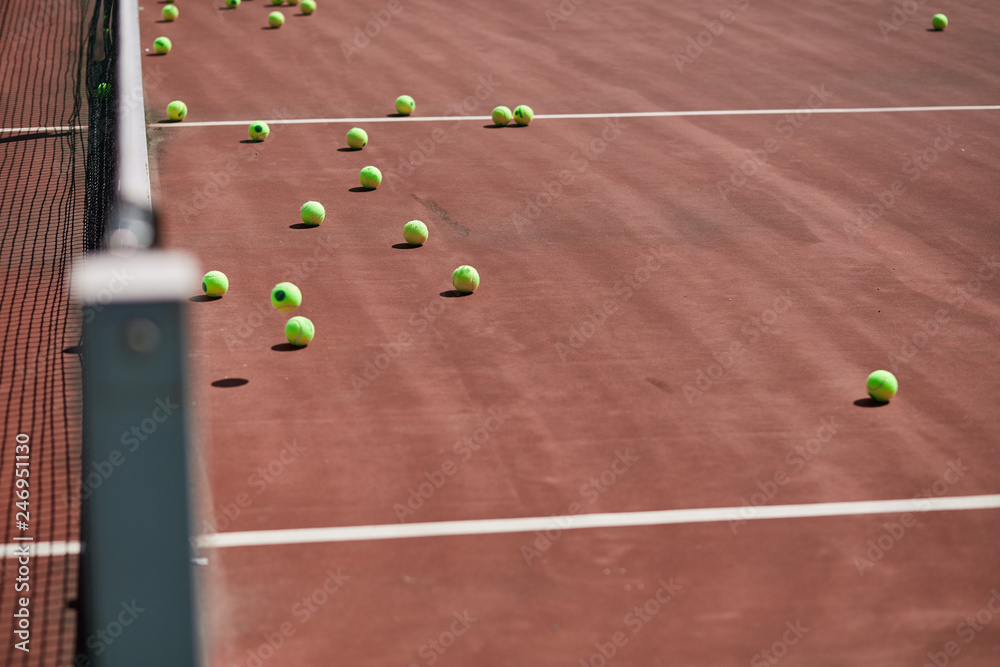 Red-clay tennis court with sport equipment and tennis balls on it. Nobody is on field
