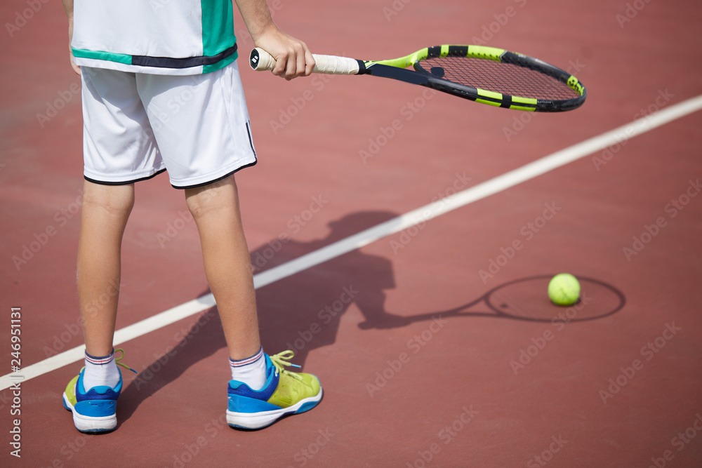 Close-up of boy s hand holding tennis ball and racket on red-clay court. Professional tennis player starting set.
