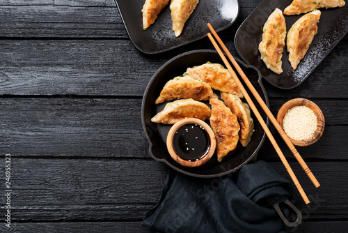 Fried dumplings Gyoza in a frying pan, soy sauce, and chopsticks on a black wooden background, top view 