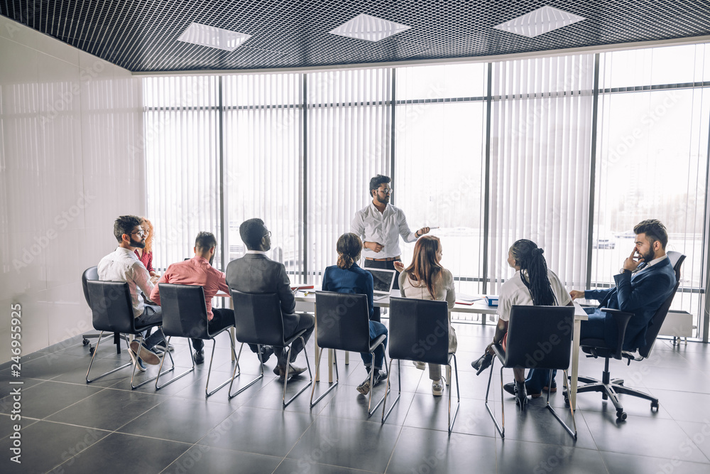 Achieving best results after annual refresher course. Indian young business mentor conducting a business training while standing in front of people sitting in row at meeting room. Achieving best results after annual refresher course. Indian young business mentor conducting a business training while standing in front of people sitting in row at meeting room.