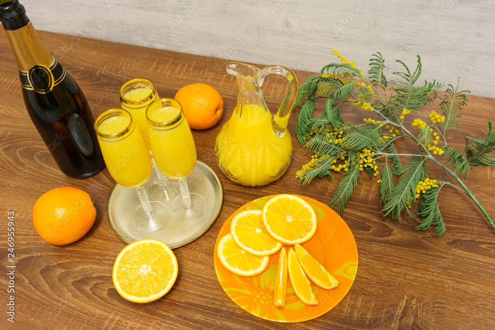 Three glasses of mimosa cocktail, a bottle of champagne, a decanter with  orange juice, fresh oranges and mimosa sprig on a wooden table Stock Photo  | Adobe Stock