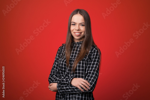 Beautiful young woman smiling with hands folded, looking at camera isolated over red background